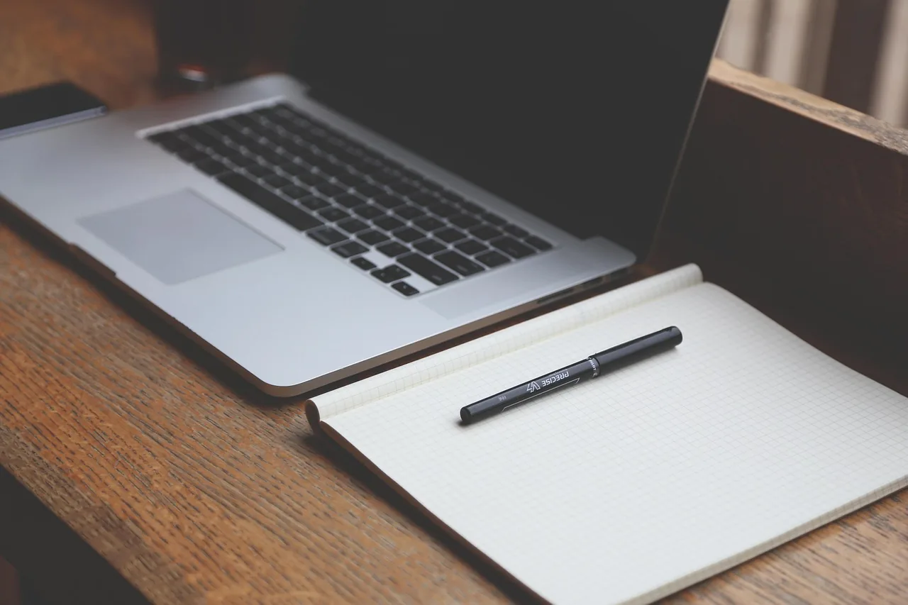 Ordinateur portable ouvert sur un bureau en bois, à côté d'un carnet et d'un stylo