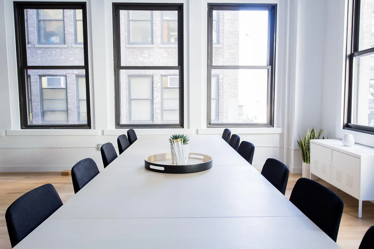 Longue table de réunion vide devant une rangée de fenêtres à petits carreaux