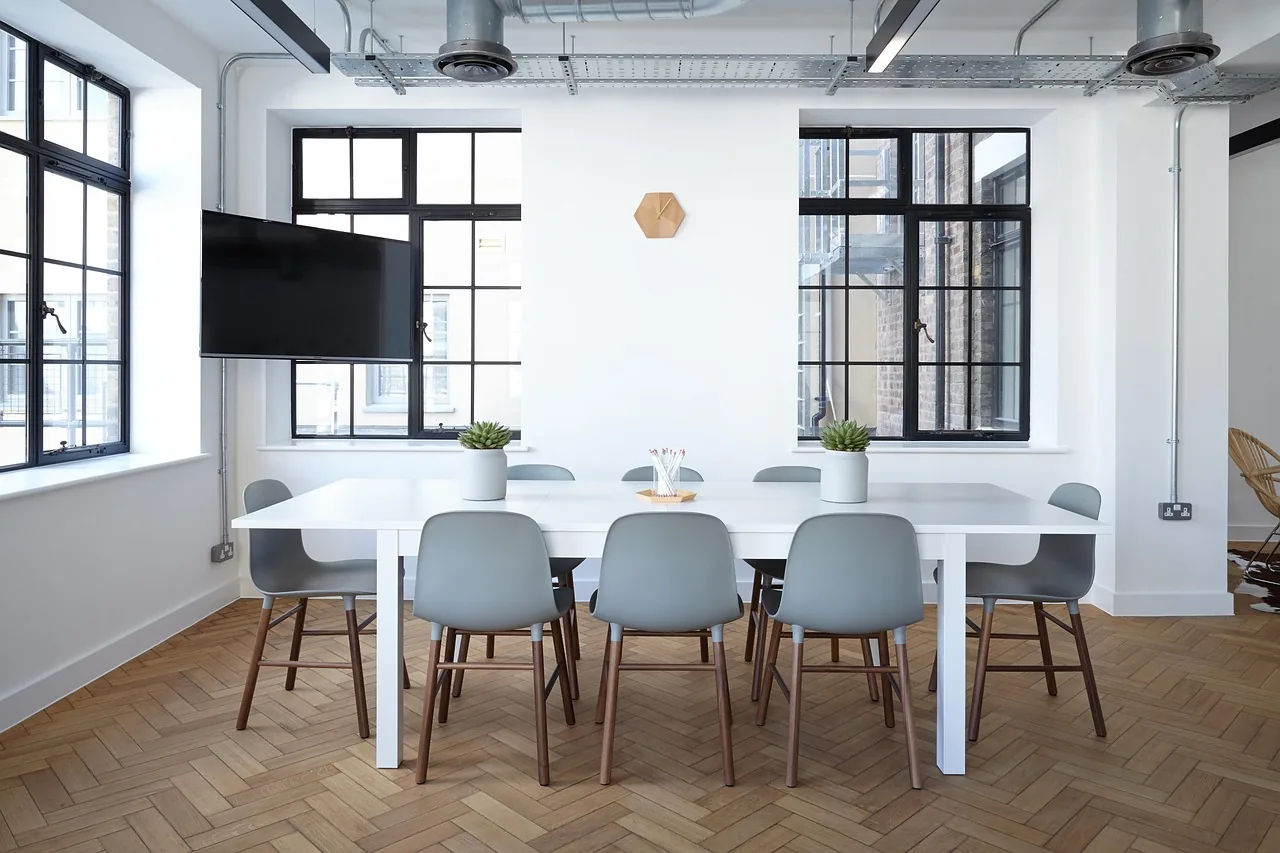 Salle de réunion claire avec une grande table et des chaises, devant de hautes fenêtres